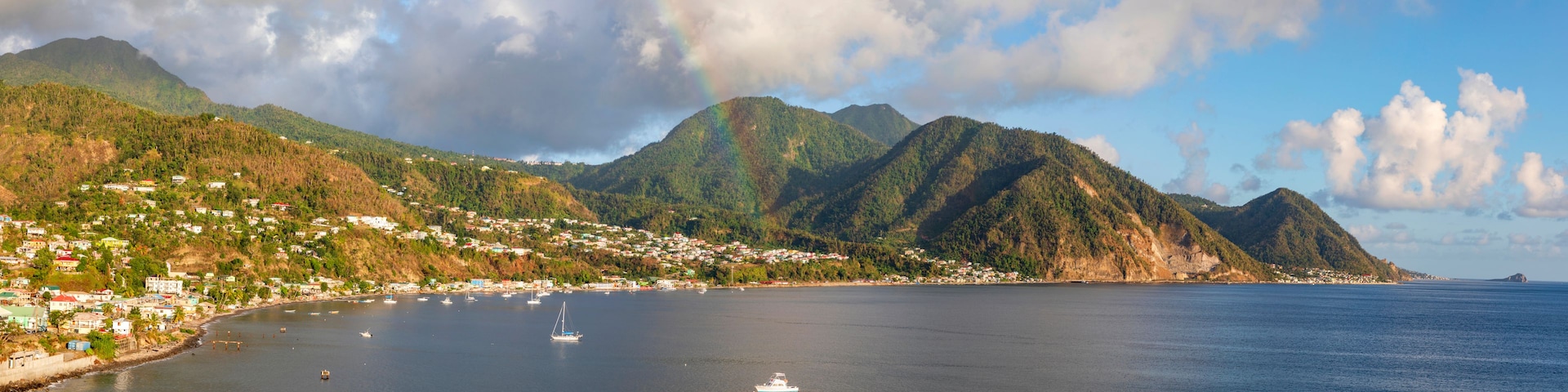 A coastal town with houses along the shore, a bay with boats, and mountains in the background.