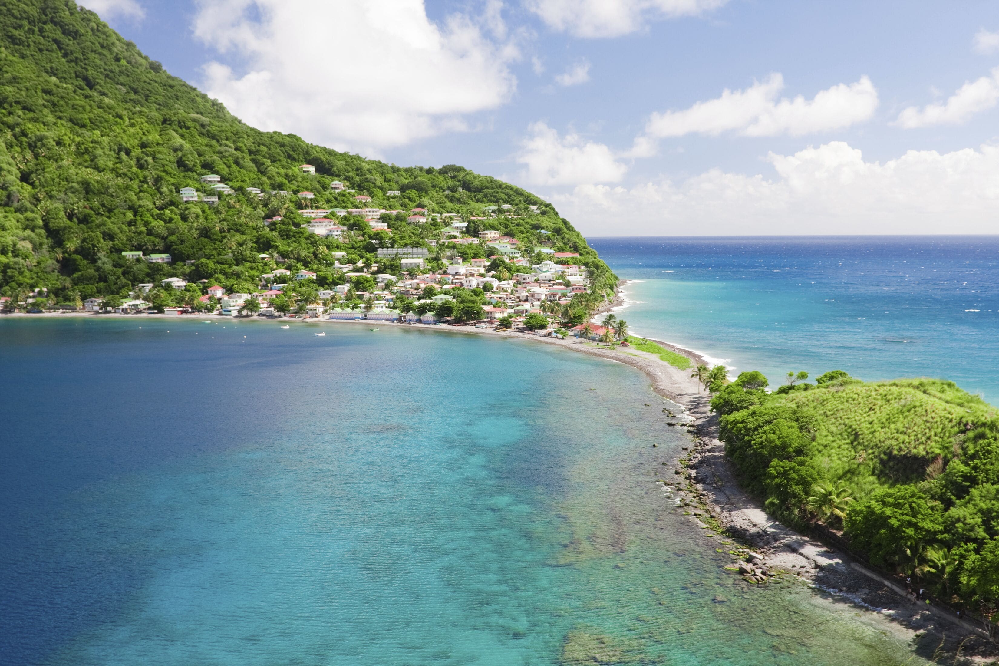 A coastal town with a clear blue sea, a green hillside, and a beach.