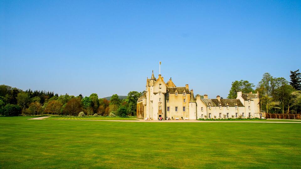 A large castle with a green lawn in front.