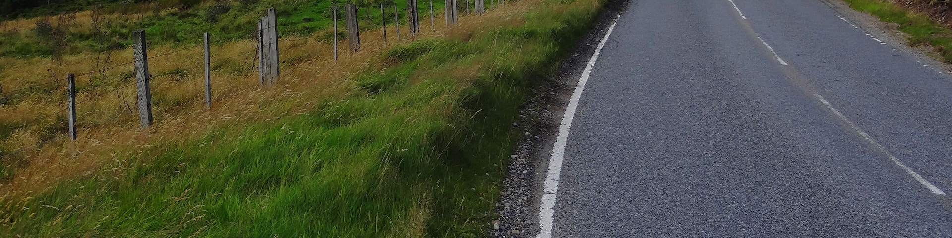 A rural road flanked by rolling hills and sparse vegetation.