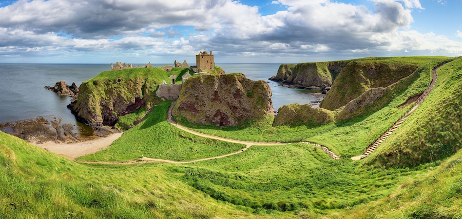 A coastal landscape with a castle on a cliff, green hills, and a winding path.