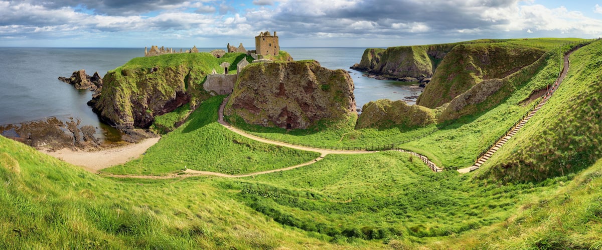 A coastal landscape with a castle on a cliff, green hills, and a winding path.