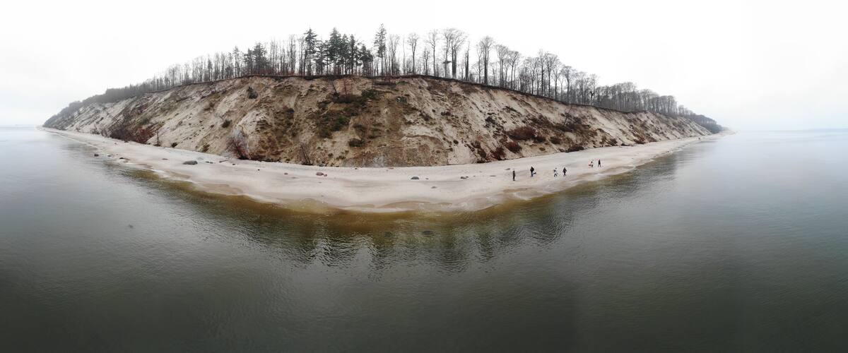 A snow-covered island with a forested cliff and a sandy beach.