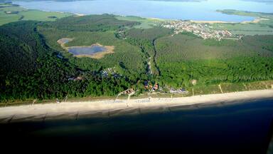 An aerial view of a coastal area with a beach, dense forest, a small town, and a large body of water.