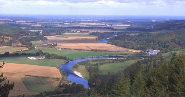 A river winding through a valley with fields and a forested area.