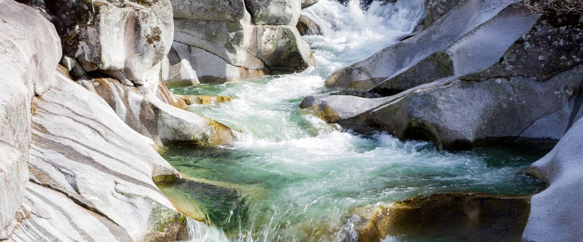 A river flowing through a rocky gorge with clear water and large boulders.