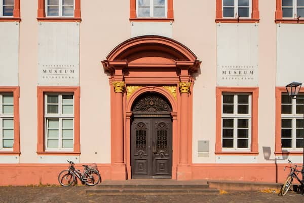 Un bâtiment rose avec une porte noire, deux vélos garés devant, et une enseigne indiquant « Musée de l’université de Heidelberg ».