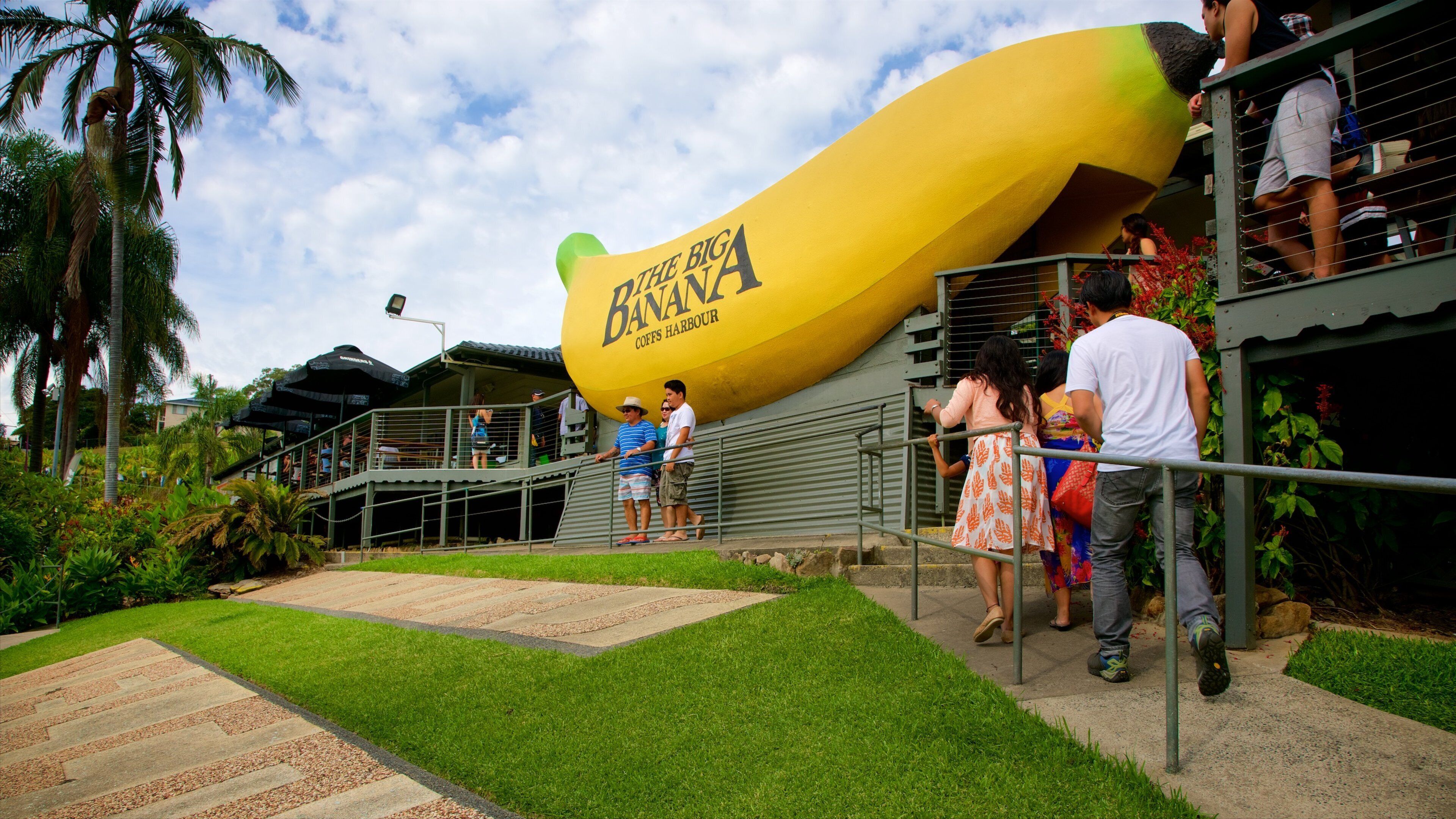 A large banana sculpture at a tourist attraction with people walking around.