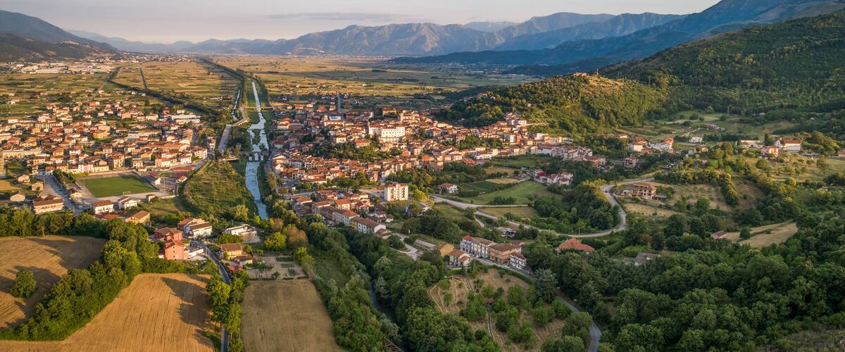 An aerial view of a town nestled in a valley with a river running through it, surrounded by hills and mountains.