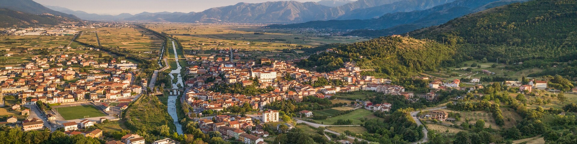 An aerial view of a town nestled in a valley with a river running through it, surrounded by hills and mountains.
