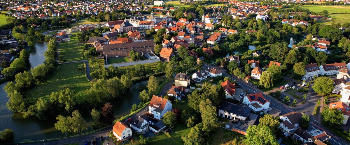 An aerial view of a town with a river, green fields, and wind turbines in the distance.