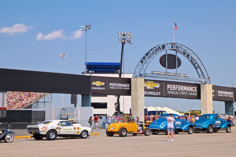 A vintage car show with classic cars parked in front of a Chevrolet Performance banner.