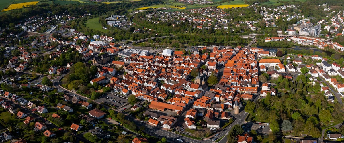 An aerial view of a town with red-roofed houses, a river, and surrounding green fields.