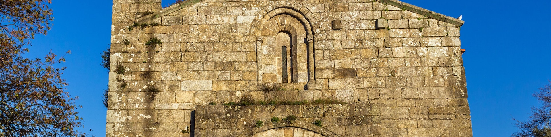 A stone church with a prominent arched entrance and a cross on the roof.