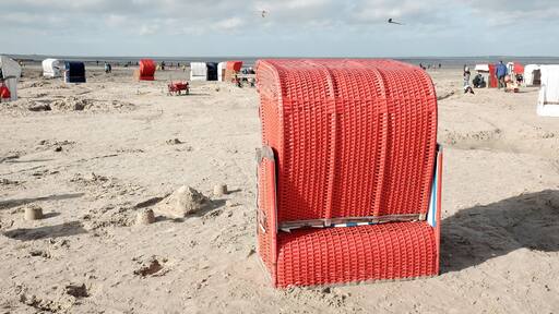 Roter Strandkorb am Strand von Bensersiel im Herbst bei Sonnenschein an der Küste der Nordsee bei Esens in Ostfriesland in Niedersachsen