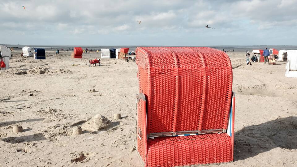 A beach with red and white beach huts, a sandy shore, and a cloudy sky.