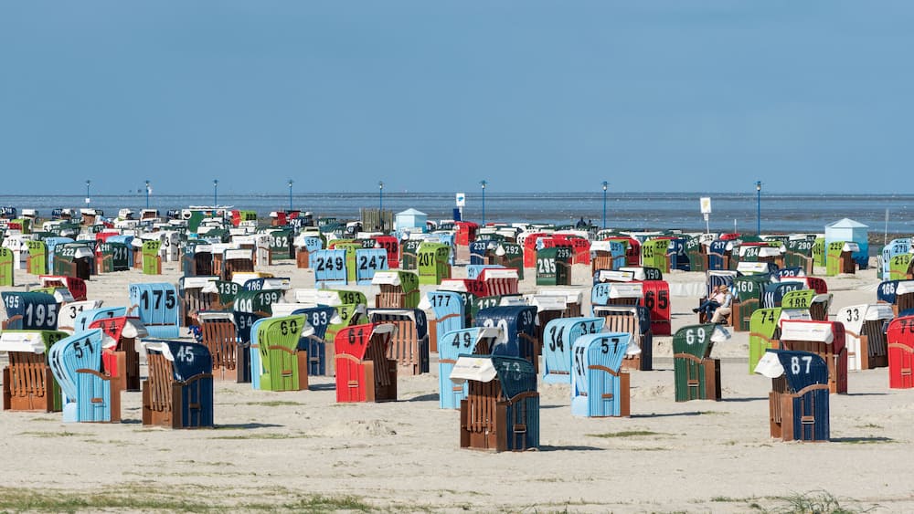Une plage où l’on trouve de nombreuses cabanes de plage aux couleurs vives, chacune étant numérotée pour faciliter son identification.