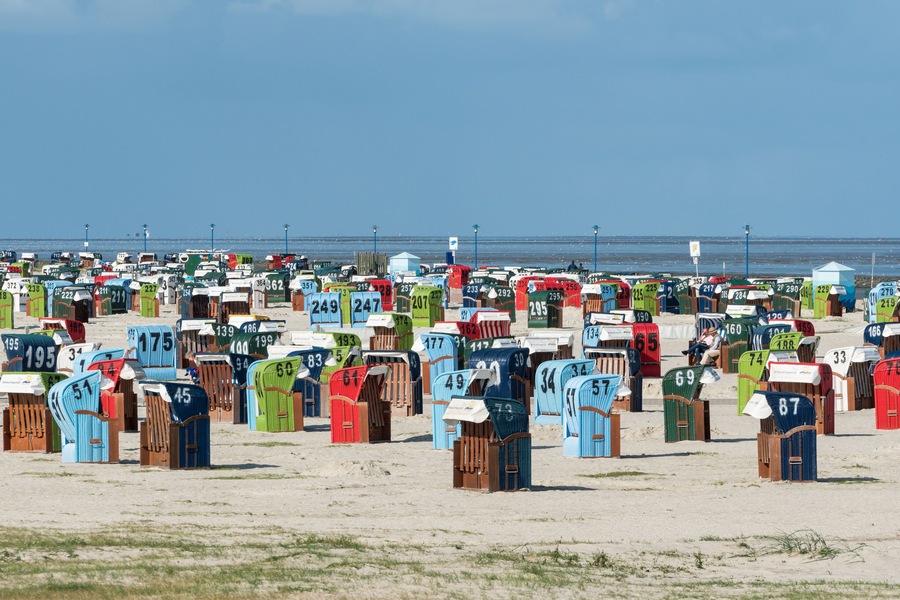 Ein Strand mit zahlreichen bunten Strandkörben, die zur Unterscheidung nummeriert sind.