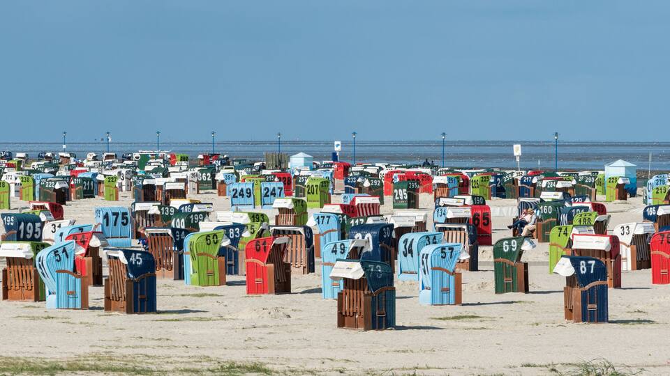 A beach with numerous colorful beach huts numbered for identification.