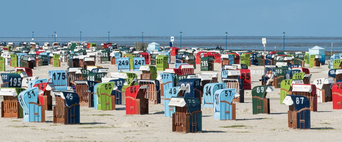 A beach with numerous colorful beach huts numbered for identification.