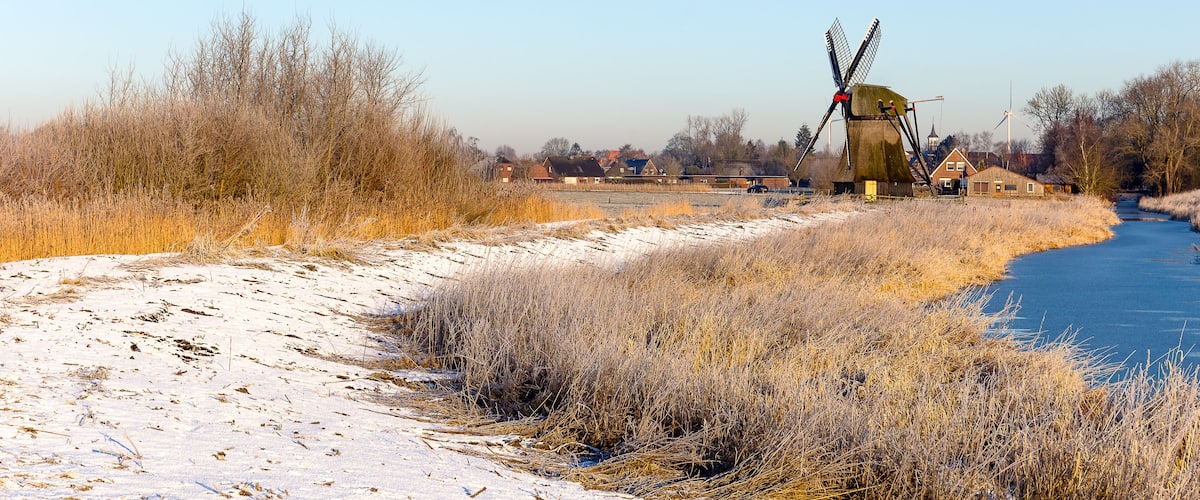 A windmill, a river, and houses in a rural area.