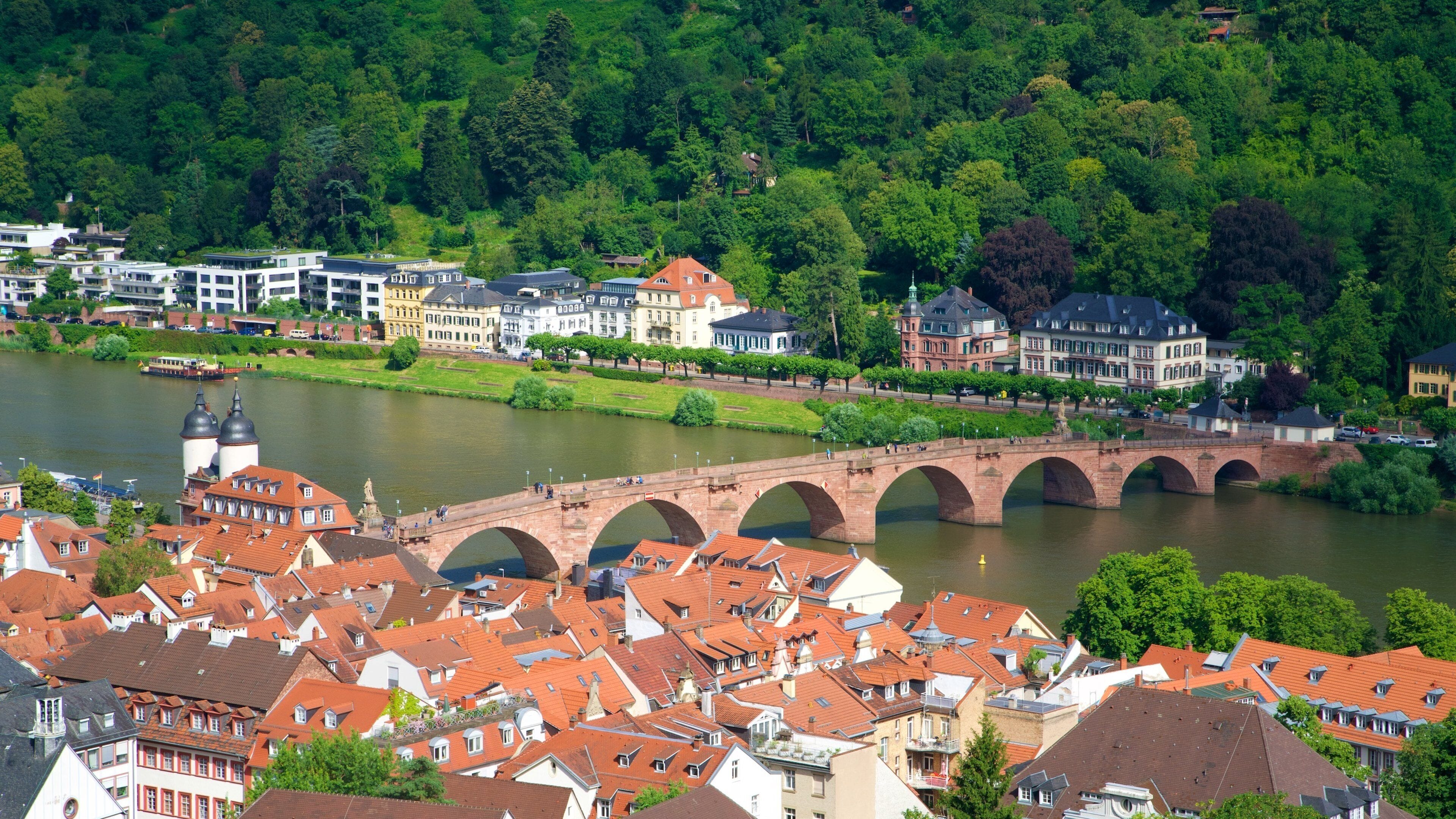 A river with a stone bridge, surrounded by buildings and greenery.
