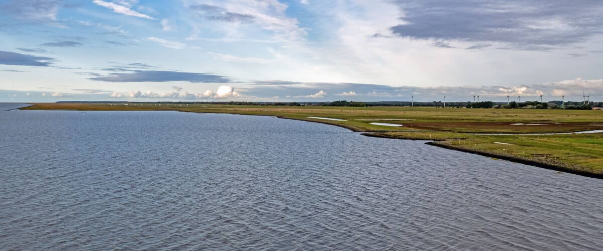 A river curving through a landscape with grassy fields and wind turbines in the distance.