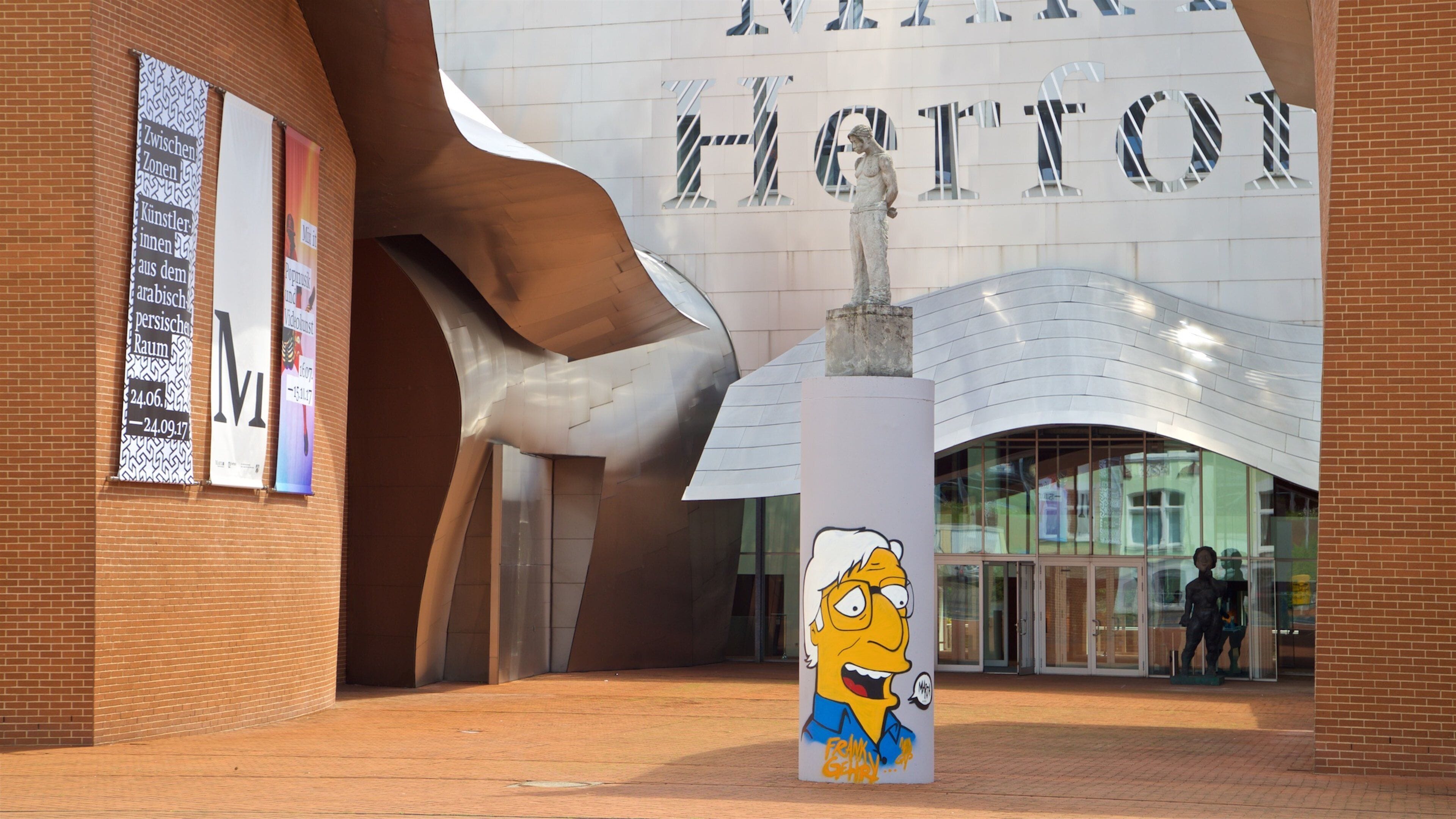 A modern building with a large sculpture and a Simpsons character statue.