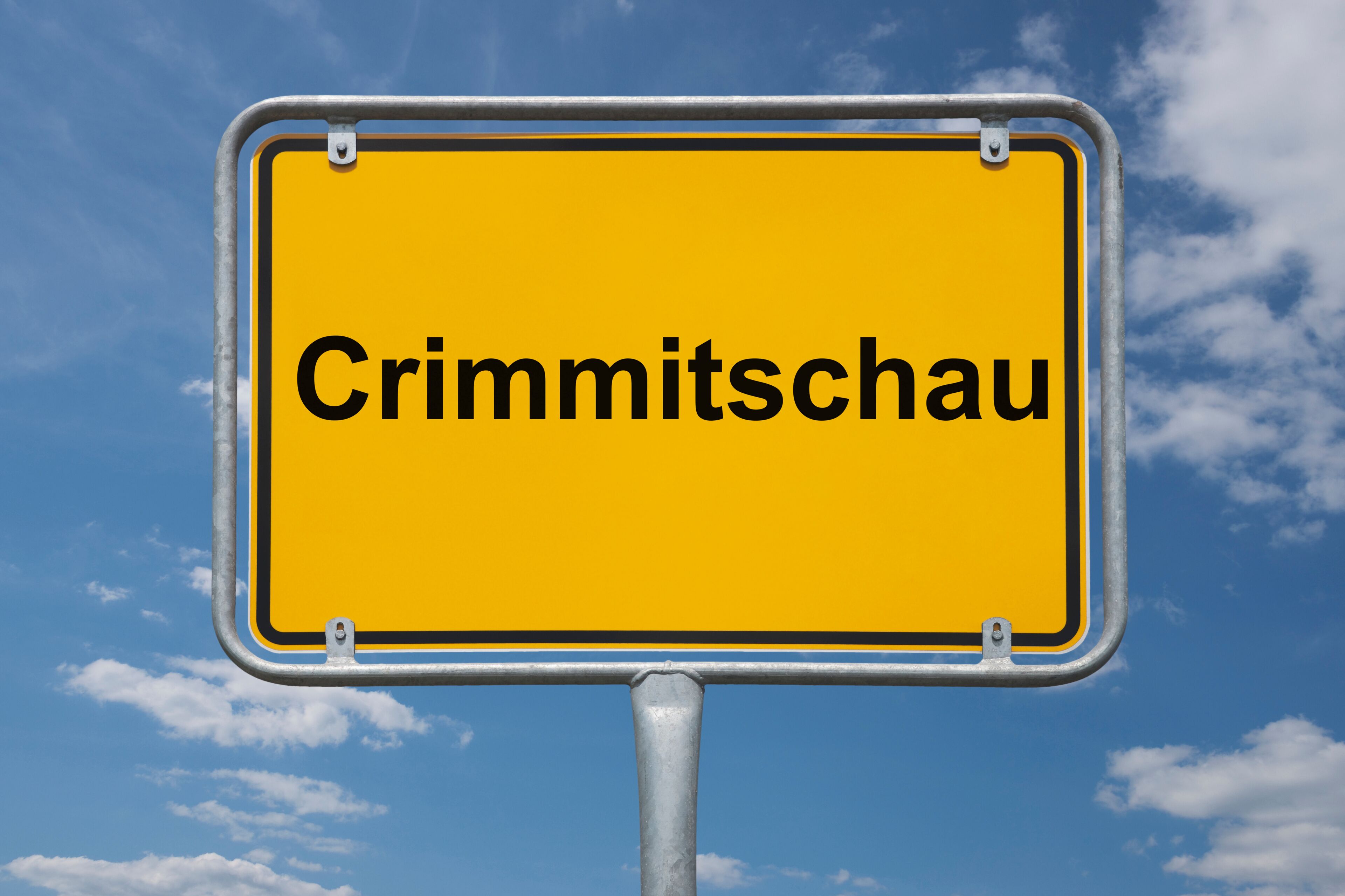 A yellow sign with the text "Crimmitschau" against a blue sky with clouds.