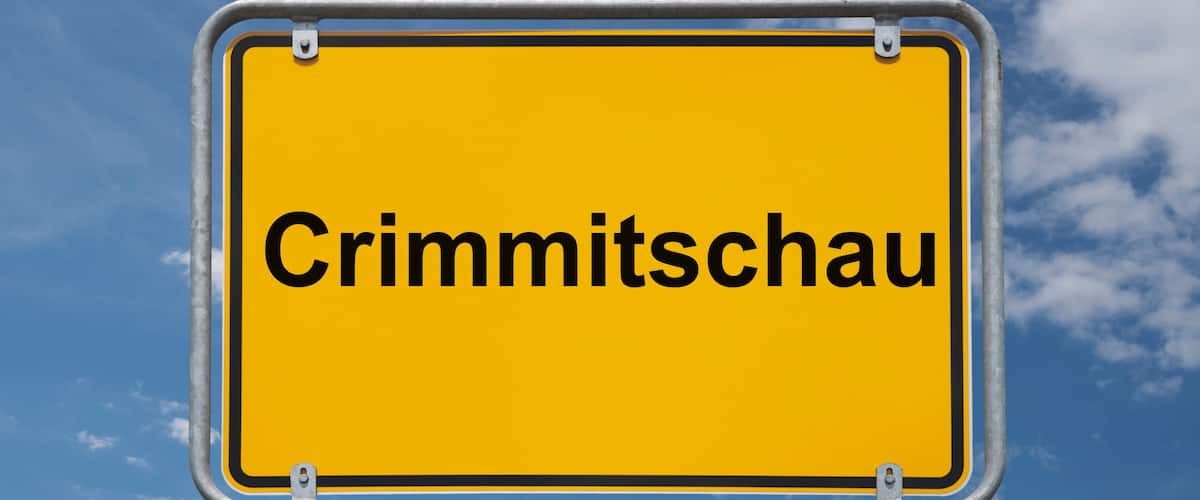 A yellow sign with the text "Crimmitschau" against a blue sky with clouds.