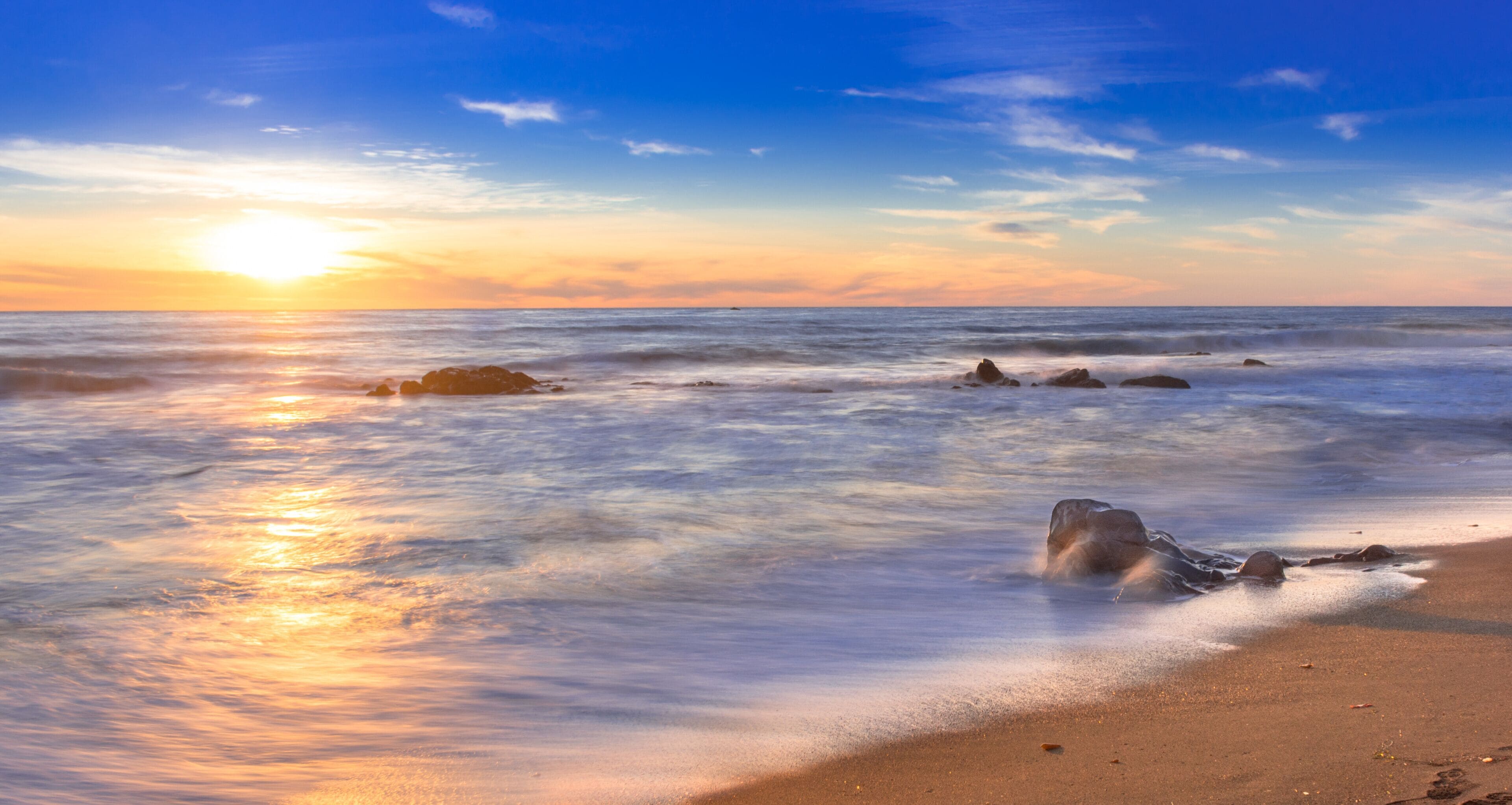 Une plage avec des vagues, des rochers et un coucher de soleil.
