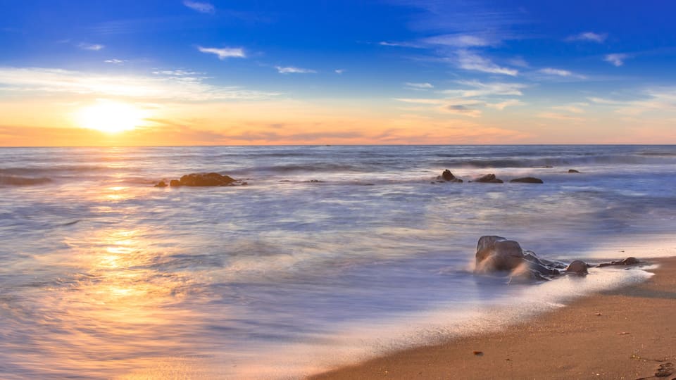 A beach with waves, rocks, and a sunset.