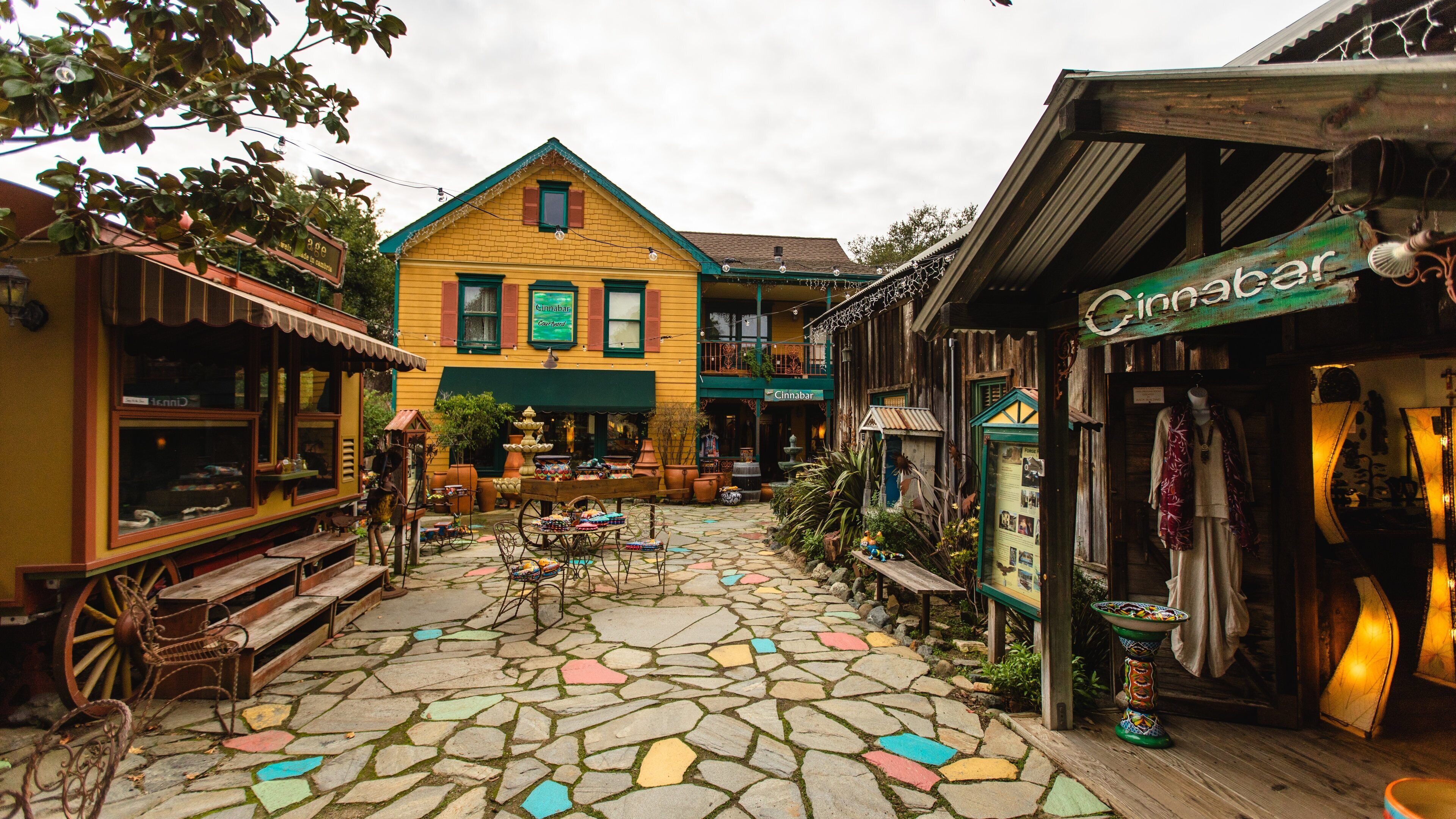 A colorful courtyard with a yellow building, a wooden bench, and a shop with a sign reading "Cinnabar".