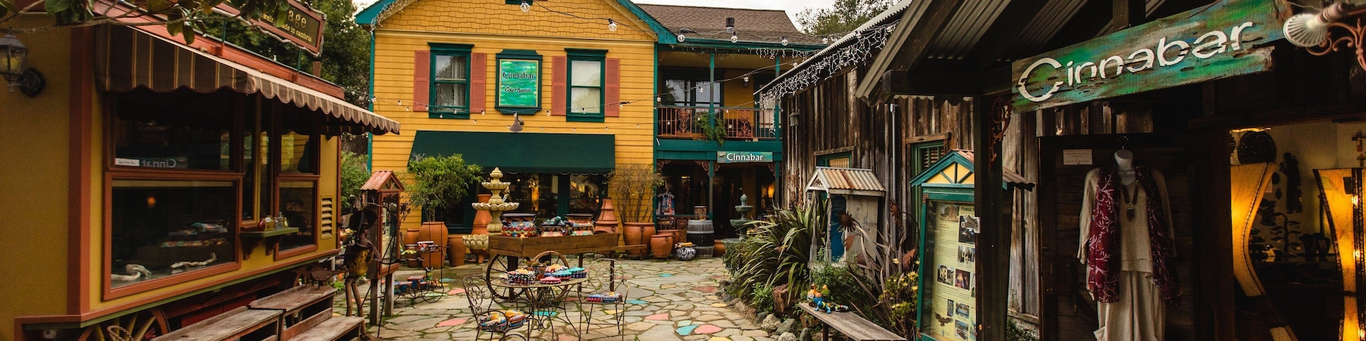 A colorful courtyard with a yellow building, a wooden bench, and a shop with a sign reading "Cinnabar".