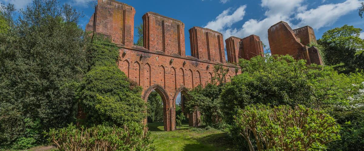 A historic brick structure with arches and towers, surrounded by lush greenery.