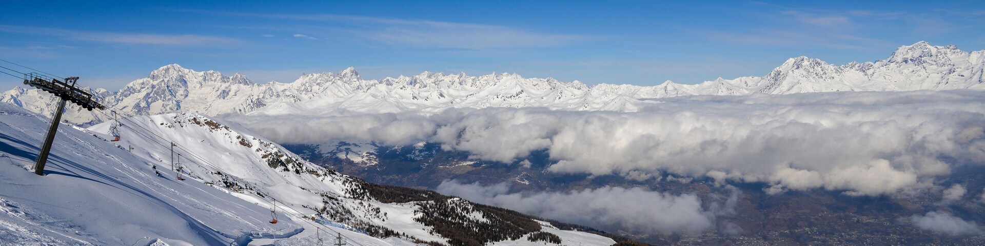 Chairlift at Italian ski area of Pila on snow covered Alps and pine trees during the winter with Mt. Blanc in France visible in background