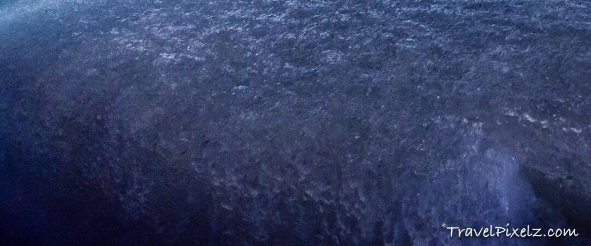 A crowd of people observing a large ice formation in a cave.
