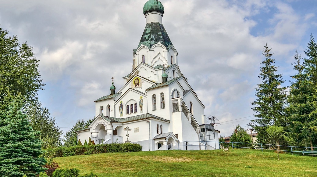 A white church with a green dome and crosses, surrounded by trees and grass.