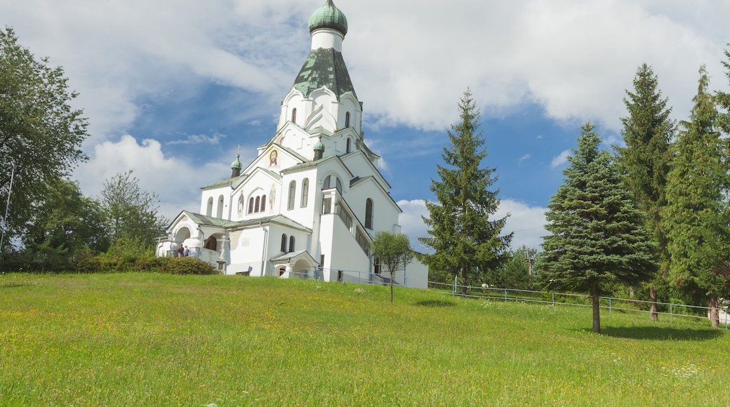 A white church with a green dome and cross, surrounded by trees and grass.