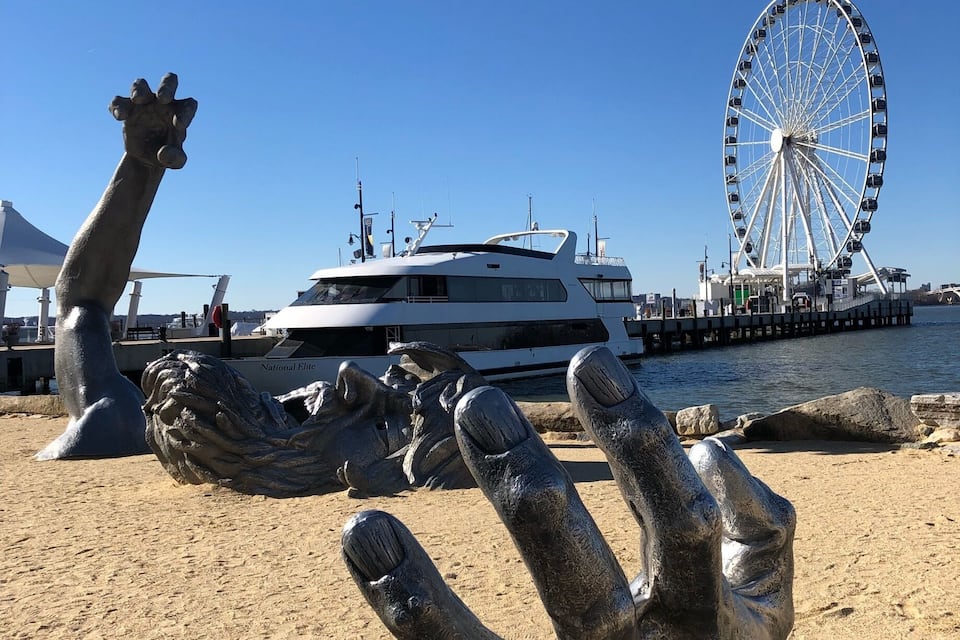 Une plage avec une grande roue, un yacht et une sculpture représentant une main.
