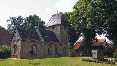 A historic stone church with a tower, surrounded by a well-maintained lawn and mature trees.