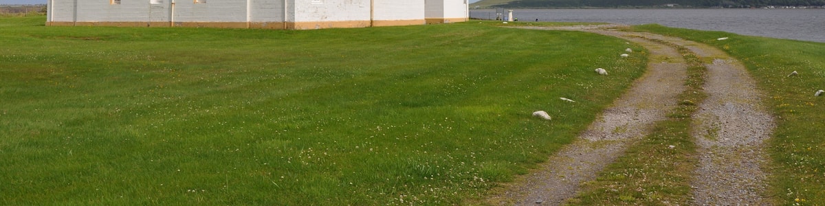 A lighthouse with a white and yellow exterior, a single-story building, and a clear path leading to it.
