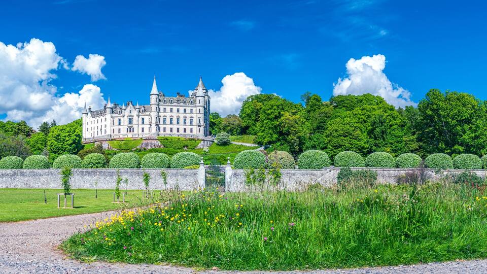 A grand castle surrounded by lush greenery and a well-maintained garden.