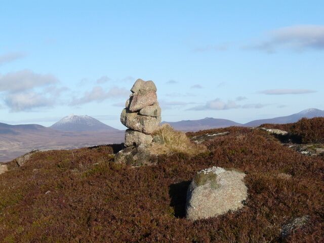 A rocky outcrop with a cairn on a hillside, surrounded by heather and distant mountains.