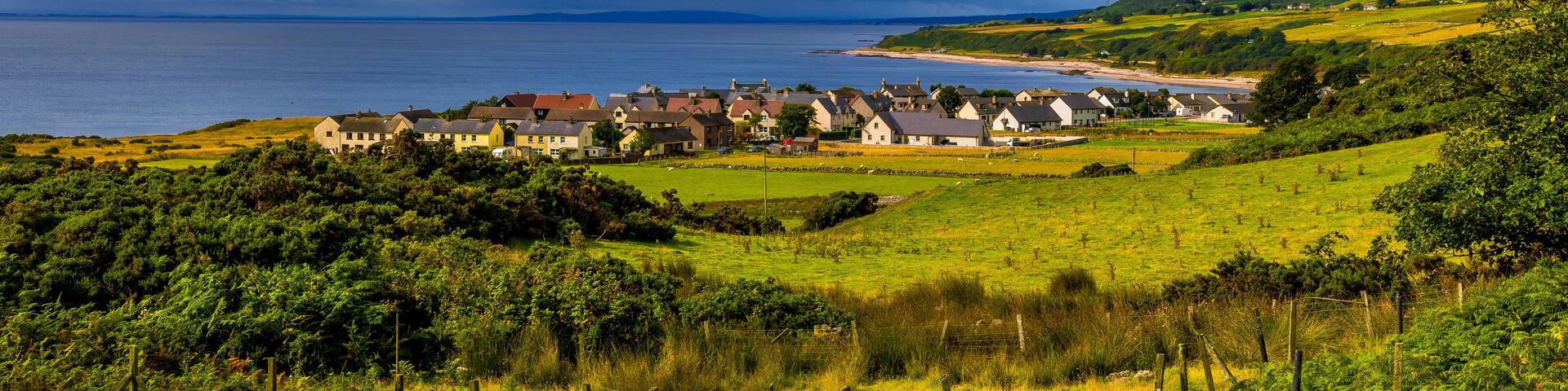 A coastal village with houses, a beach, and rolling hills.