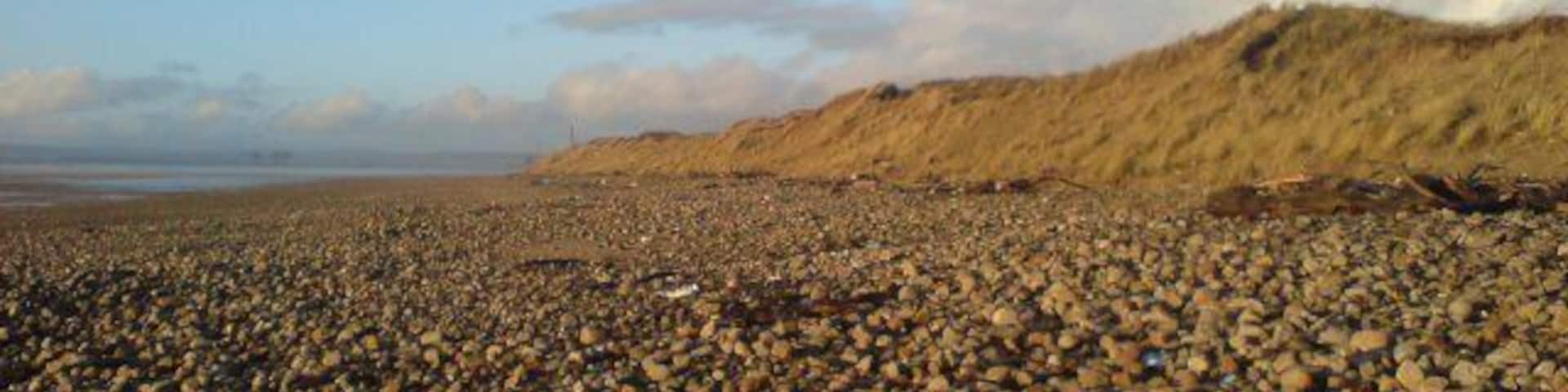 Shore at Kenfig nature Reserve Kenfig Nature Reserve is a large area of sand dunes and buroughs. The three dark structures visible in the distance are cranes, part of Margam steel works. On the map, this area is described as Kenfig Sands - those are pretty big sand grains though...