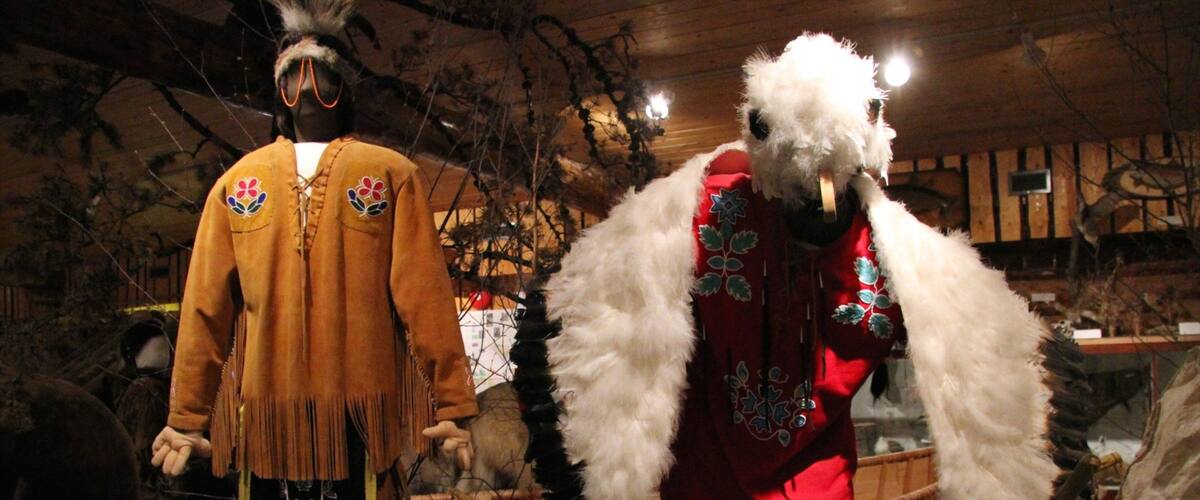 Two mannequins dressed in traditional attire, one in a brown outfit with fringe and the other in a red outfit with white fur.