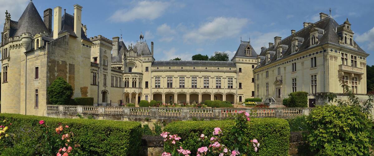 A large, historic castle with multiple towers and a well-maintained garden with pink flowers.
