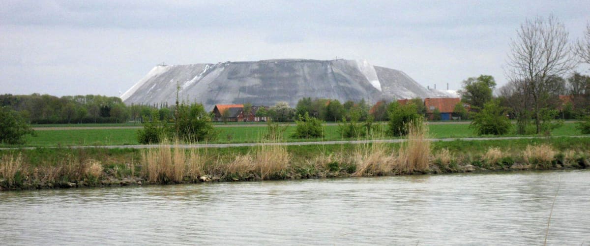 A large hill with a building in the foreground and a river in the foreground.