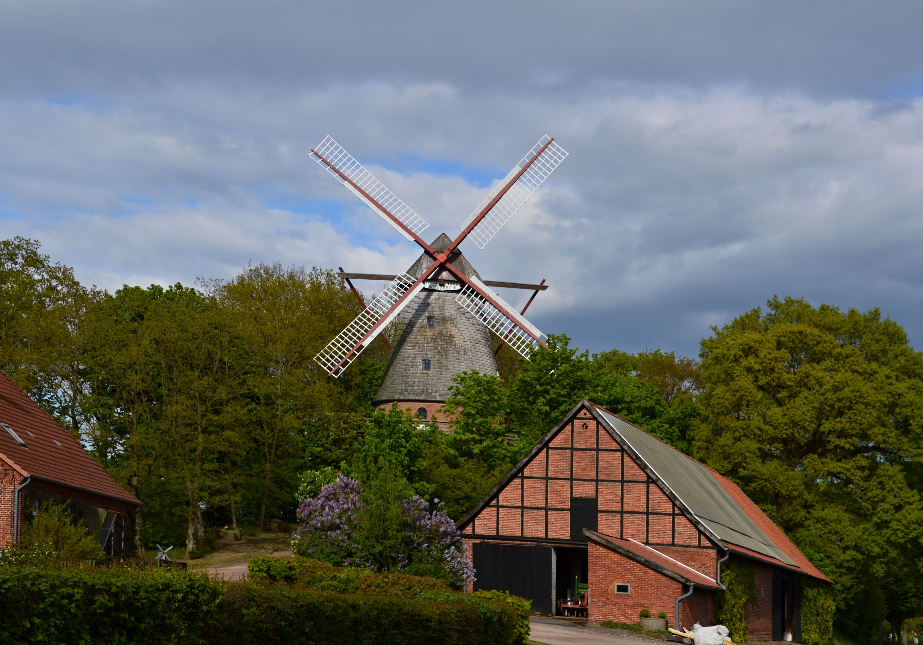 A traditional windmill surrounded by lush greenery and a small brick building.